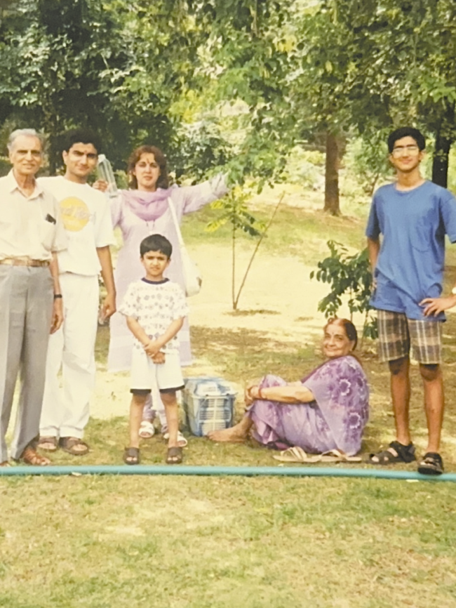 Family posing outdoors in a park-like setting with trees and grass.